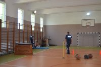 sala gimnastyczna, na której widać dwóch policjantów oraz mężczyznę w stroju sportowym wykonującego ćwiczenie z piłka lekarską