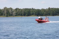 jezioro po którym płynie strażacka łódź motorowa wraz ze strażakiem i funkcjonariuszem Policji