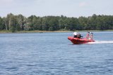 jezioro po którym płynie strażacka łódź motorowa wraz ze strażakiem i funkcjonariuszem Policji