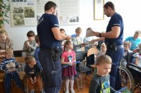 policjanci rozdają grupie dzieci odblaski i plany lekcji
