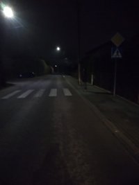 wieczór, widać ulicę i przejście dla pieszych przy którym ledwo dostrzegalny stoi pieszy na ciemno ubrany