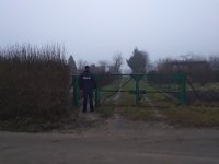 brama na terenie ogródków działkowych przy której stoi policjant