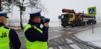 droga po której porusza się samochód ciężarowy, policjant trzyma w ręku urządzenie do pomiaru prędkości