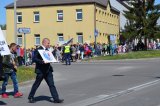 ulice miasta grupa osób idzie w pochodzie, na czele przedstawiciel Warsztatów Terapii Zajęciowej w Sejnach niesie plakat z symbolem osób niepełnosprawnych