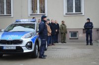 plac przy budynku komendy Policji, stoi grupa osób, nowy radiowóz i mężczyzna w mundurze policjanta przemawia